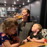 Kelli having a drink behind her kids at a restaurant