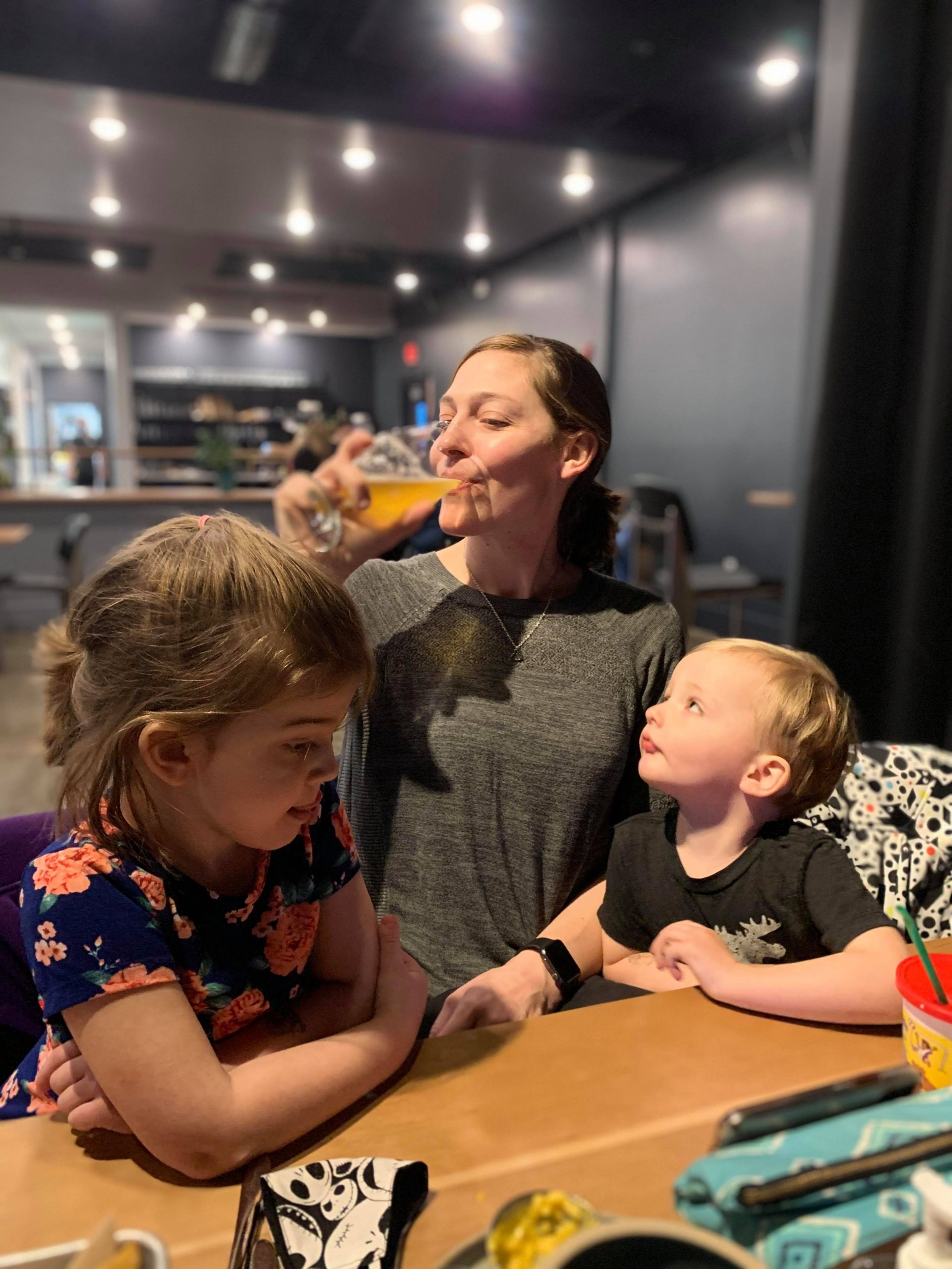 mom takes a sip of her drink behind her two kids
