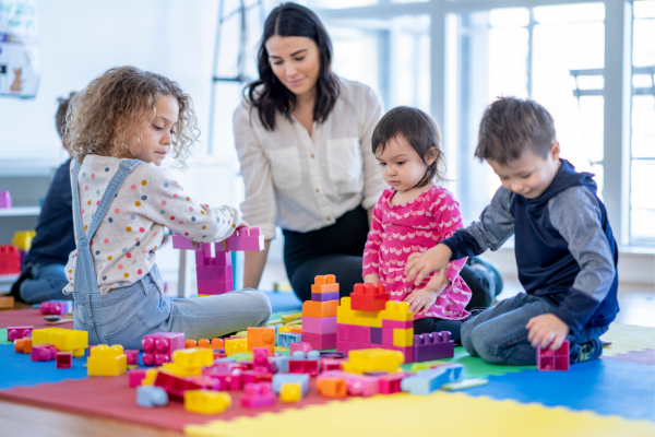 Adult with a group of toddlers that are playing with blocks.