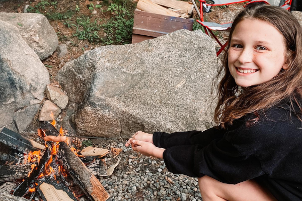 Young girl roasting a hot dog over a fire while camping