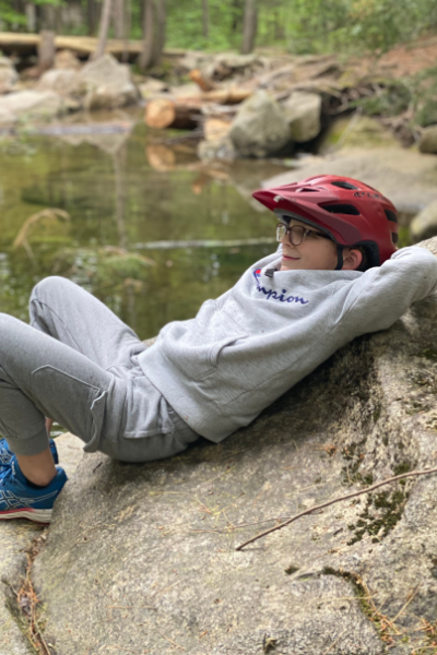 child lays on a rock by a stream while wearing a biking helmet