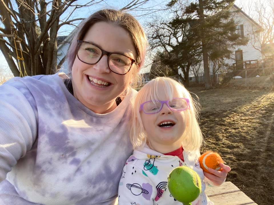 A woman and preschool child sit next to eachother, both smiley widely.