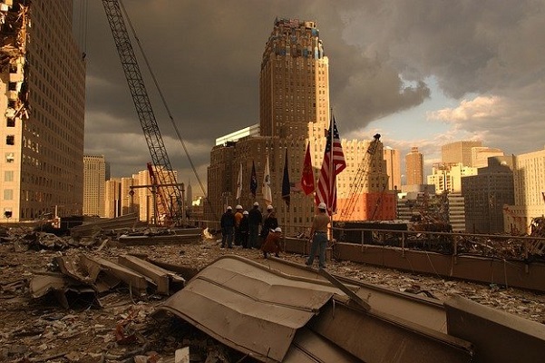 Workers stand an American flag amid the rubble of the September 11 bombing as the sun sets behind the buildings.