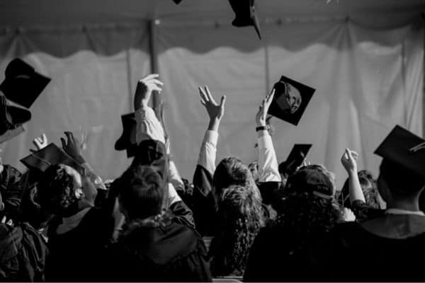 A black and white photo of graduates tossing their caps in the air after a ceremony.