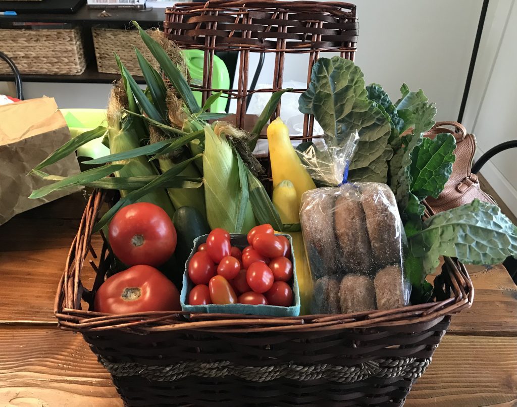 Basket full of vegetables including tomatoes, grape tomatoes, corn, squash and kale