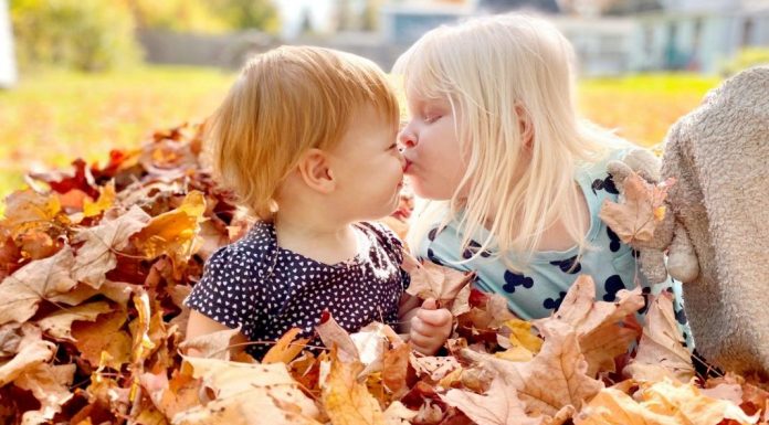 Why We’re Opting Out of Family Portraits two children sitting in a pile of leaves, one gives the other a peck on the nose