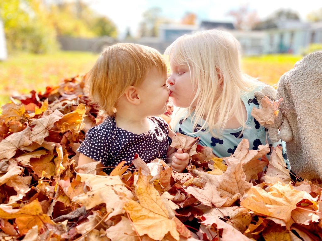 two children sitting in a pile of leaves giving a peck on the nose