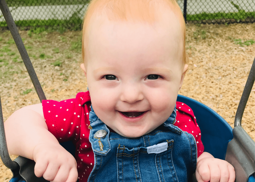 baby smiling in a bucket seat swing at a playground
