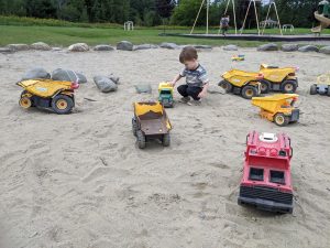 boy playing with metal toy trucks in the sand at a Vermont playground