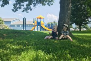 children sitting under a tree with a playground in the background