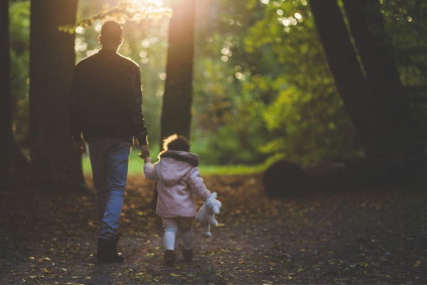 father and toddler daughter walking in the woods