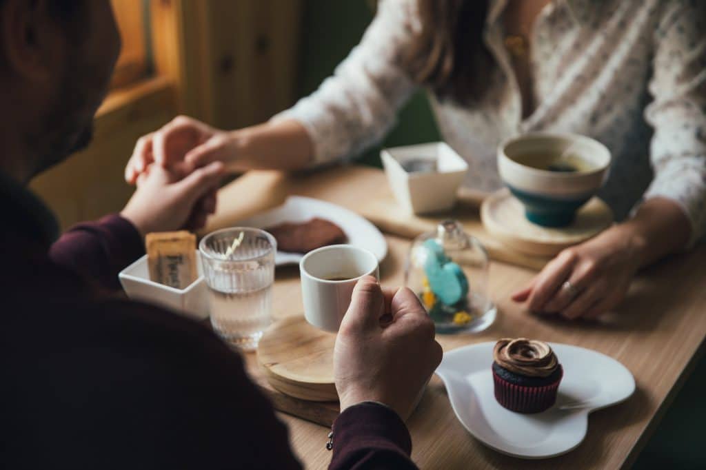 Two people holding hands accross the table with teacups and a cupcake