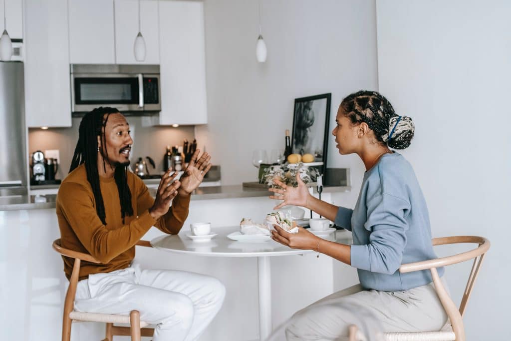 Two people arguing while sitting at a table, both using their hands to communicate.