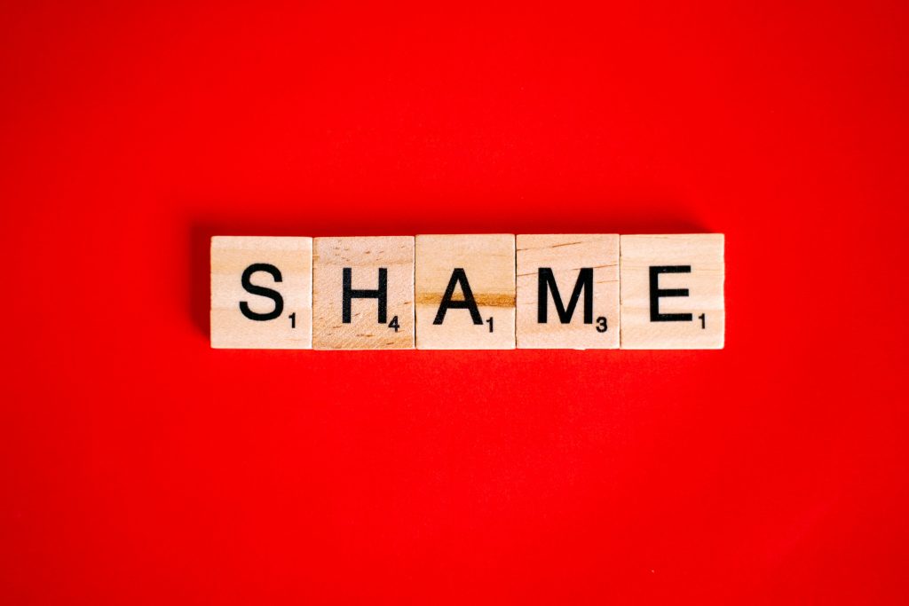 Scrabble letters spelling the word "shame" on a red background.