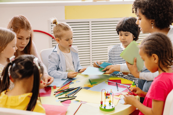 Children coloring around a table with teachers