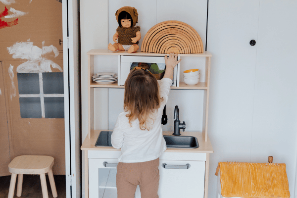 Child playing in play kitchen surrounded by toys