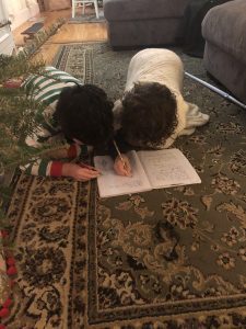 Two kids write in a notebook on the ground