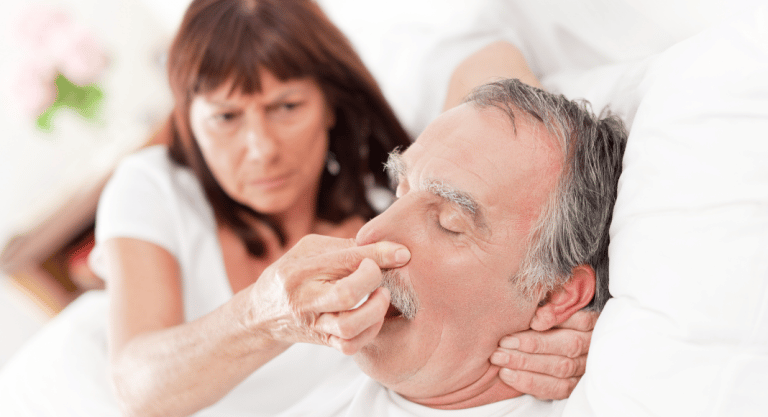 WOman plugging a sleeping man's nose