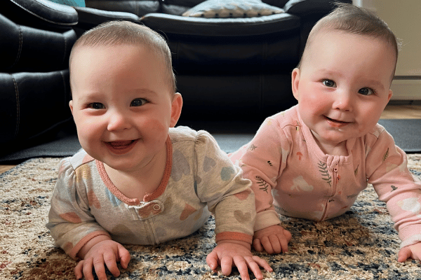 Twin baby girls grinning at the camera while enjoying tummy time