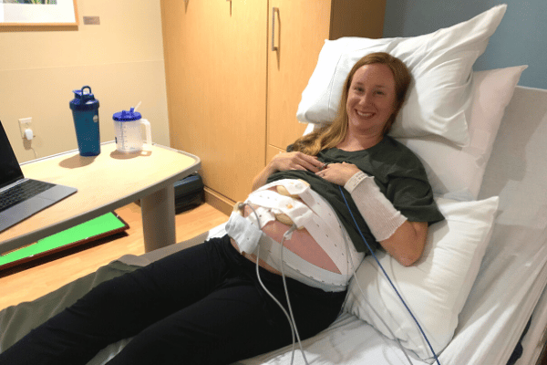 smiling blond pregnant woman in a hospital bed with wires and equipment for monitoring her pregnancy on her belly.