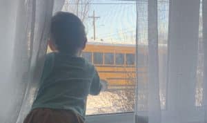 toddler looks out the window at a school bus