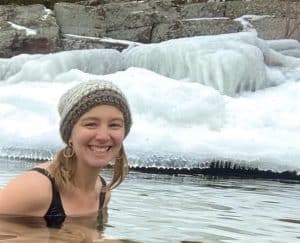Woman wading in icy water, smiling, wearing a winter hat