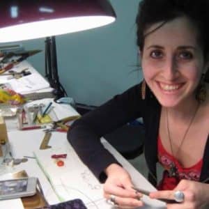woman smiles at the camera while making jewelry