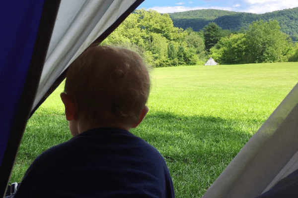 A toddler peeking out of a tent to see a green field