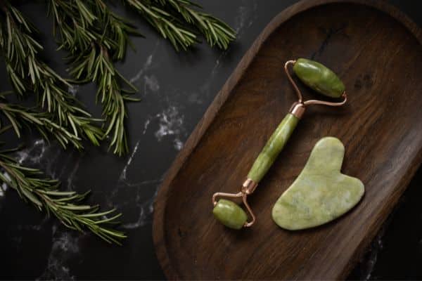 skincare tools jade roller and Gua Sha stone on wooden platter