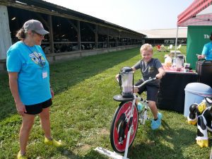 Vermont Breakfast on the Farm Volunteer in a blue shirt is watching a boy using a bike to power a blender