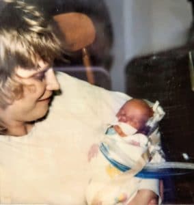 Blonde haired mother holds infant with tubes and medical equipment in rocking chair