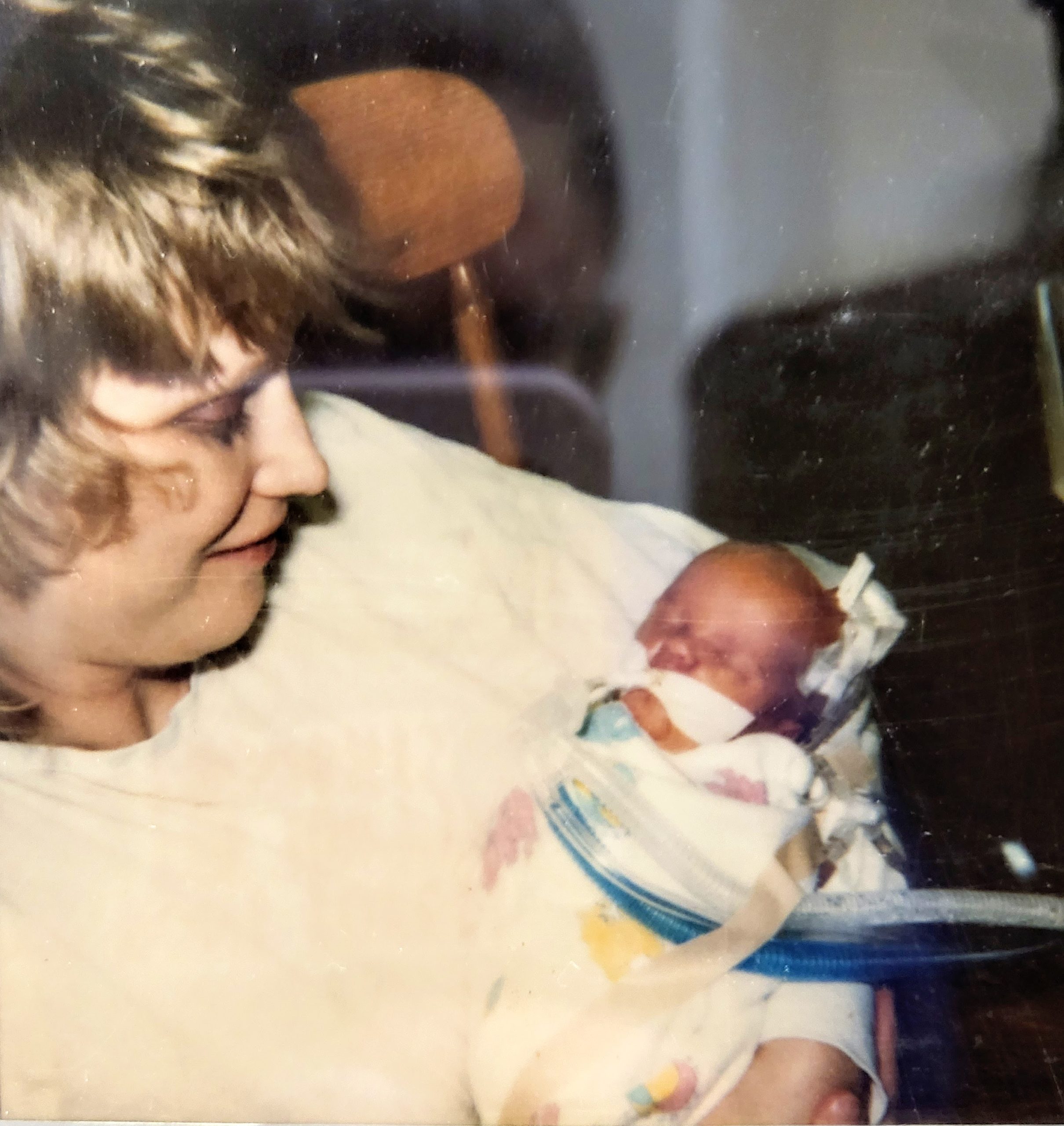 Blonde haired mother holds infant with tubes and medical equipment in rocking chair