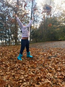 girl jumping in the leaves, stomach exposed