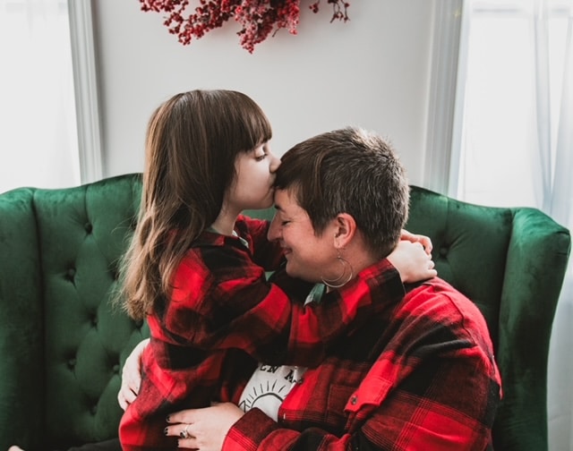 Mother and daughter embracing on a green chair. Both are wearing red and black plaid shirts.