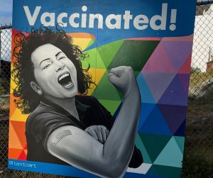 Street art with the caption "vaccinated!" and a woman making a fist