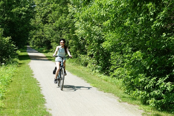 A woman on a bicycle rides down a flat rail bed trail in summer