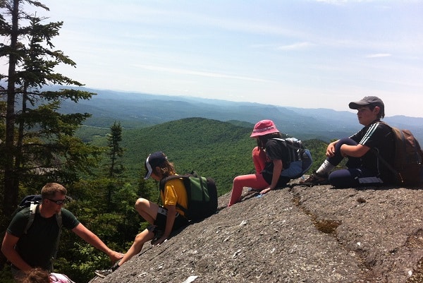 Children line up to descend a steep rock face on a mountain.