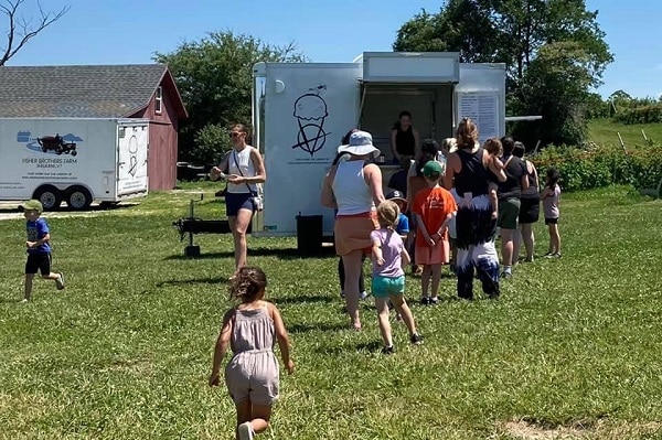 Children and families line up to get ice cream from a truck parked in a meadow.