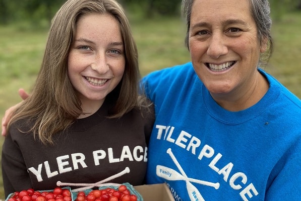 A woman and a girls smile while holding a flat of fresh picked cherries