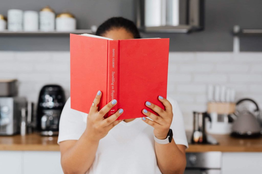 A person holding up a book with a red cover in front of their face