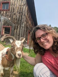 woman smiling while petting a small goat