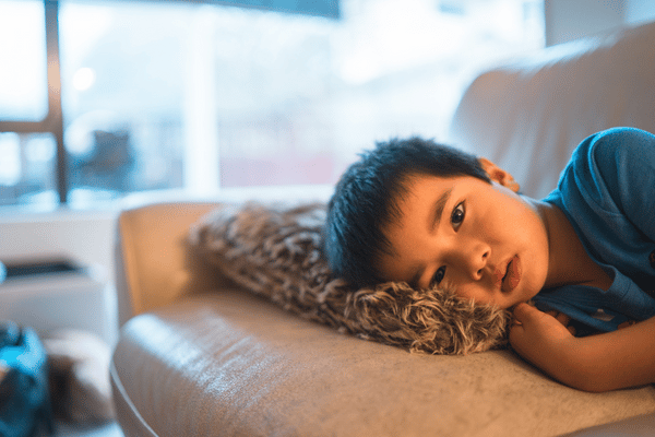 Young boy laying sadly on couch.