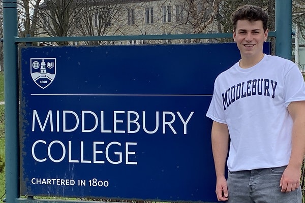 A young man stands in front of the sign to Middlebury College.