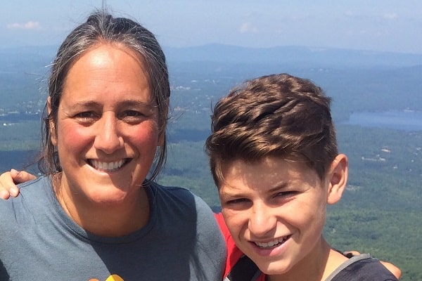 A mom and tween boy smile from the top of a mountain in summer.