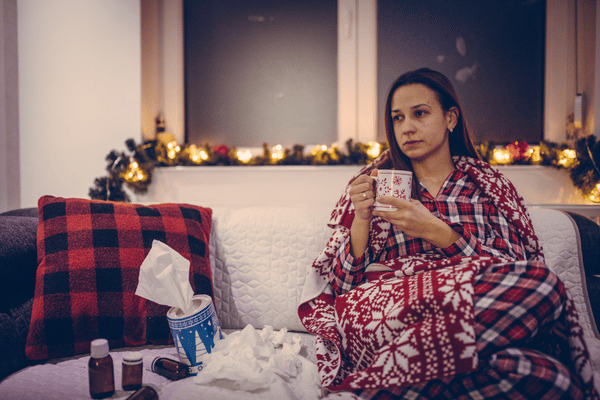 woman sits on a festively decorated couch with a cup of tea, because she is suffering from some kind of upper respiratory tract infection