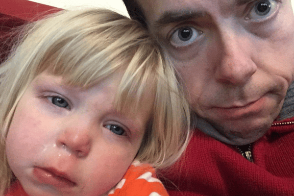 little sick girl with a snotty nose is next to her dad. She looks miserable.