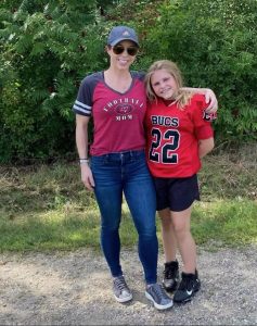 Young girl in her red touch football uniform stands next to her proud, smiling mom