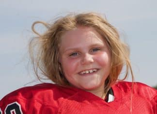 A Girl Playing Football? Meet One Who Is Dominating the Game Young girl with her hair all messed up from removing her football helmet, smiles at the camera