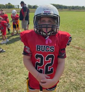 young girl peers out of a football helmet. She's wearing a red flag football uniform
