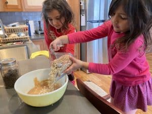 Two little girls standing on chairs at the kitchen counter making cookies